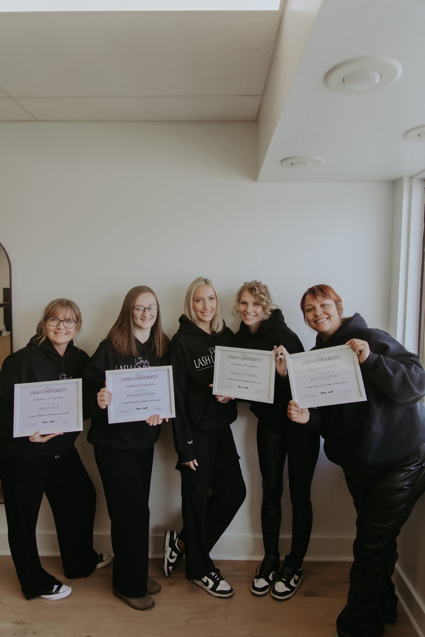 Five people in matching outfits holding certificates in a room with a white wall.