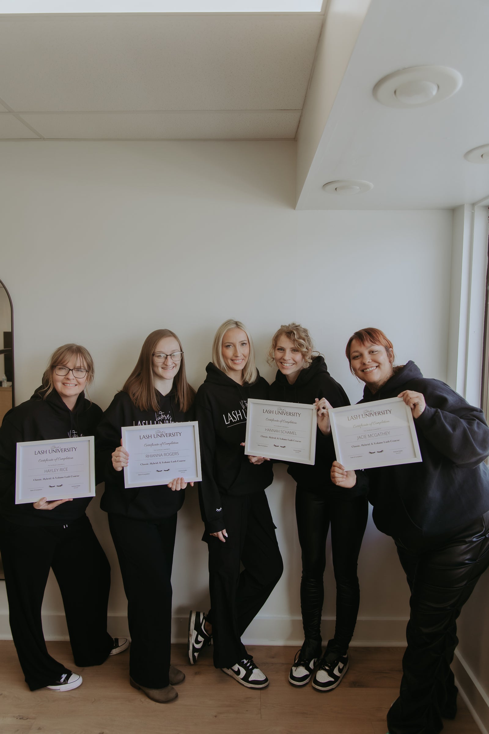 Five people in matching outfits holding certificates in a room with a white wall.