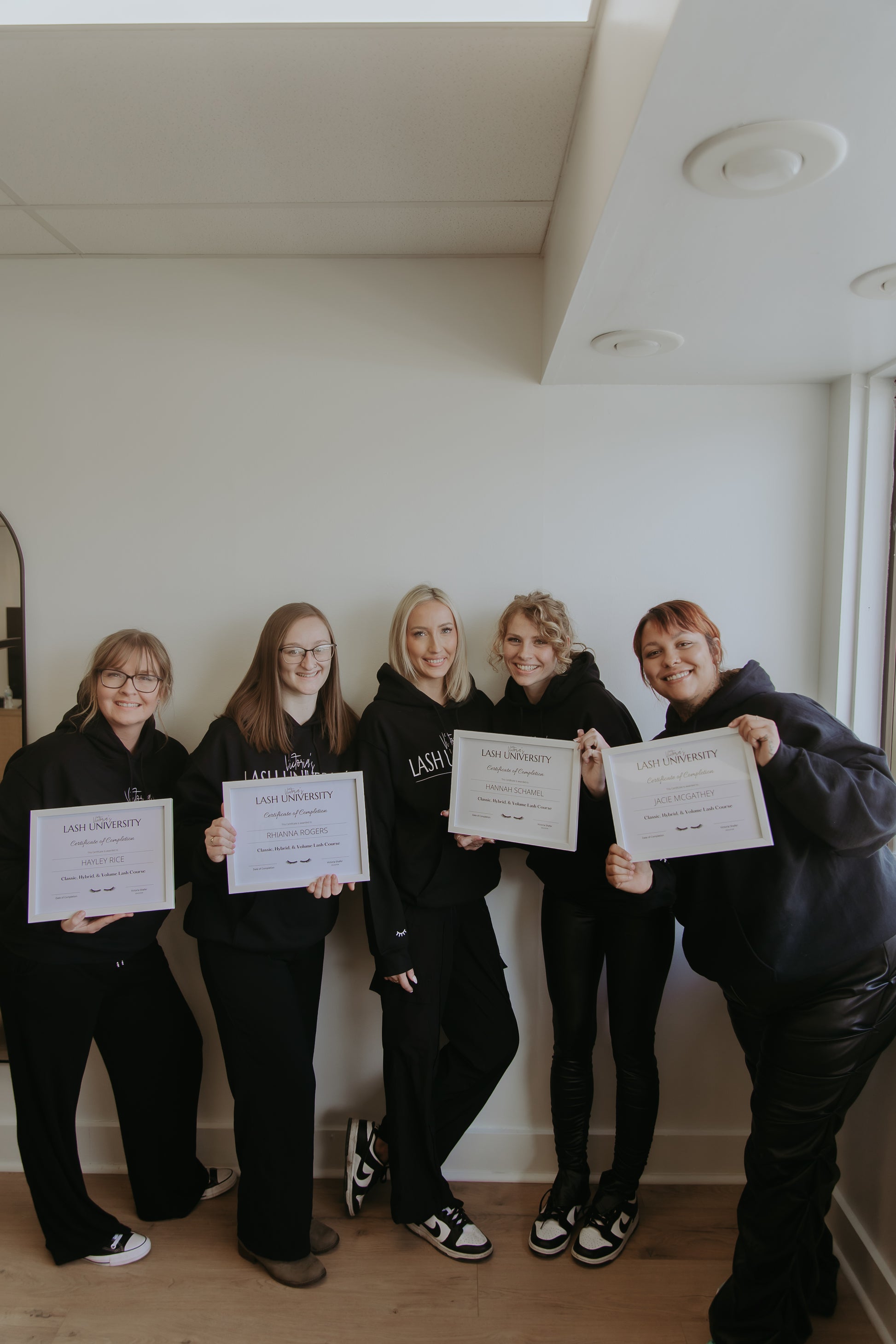 Five people in matching outfits holding certificates in a room with a white wall.