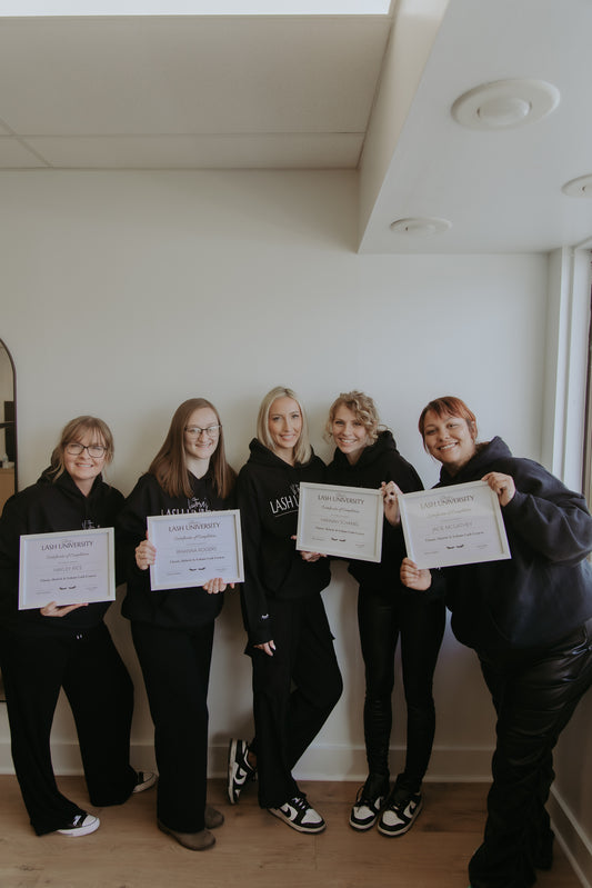 Five people in matching outfits holding certificates in a room with a white wall.